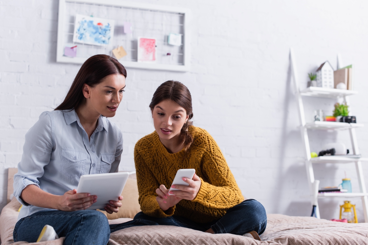 Mom on tablet with teenage daughter looking at smart phone