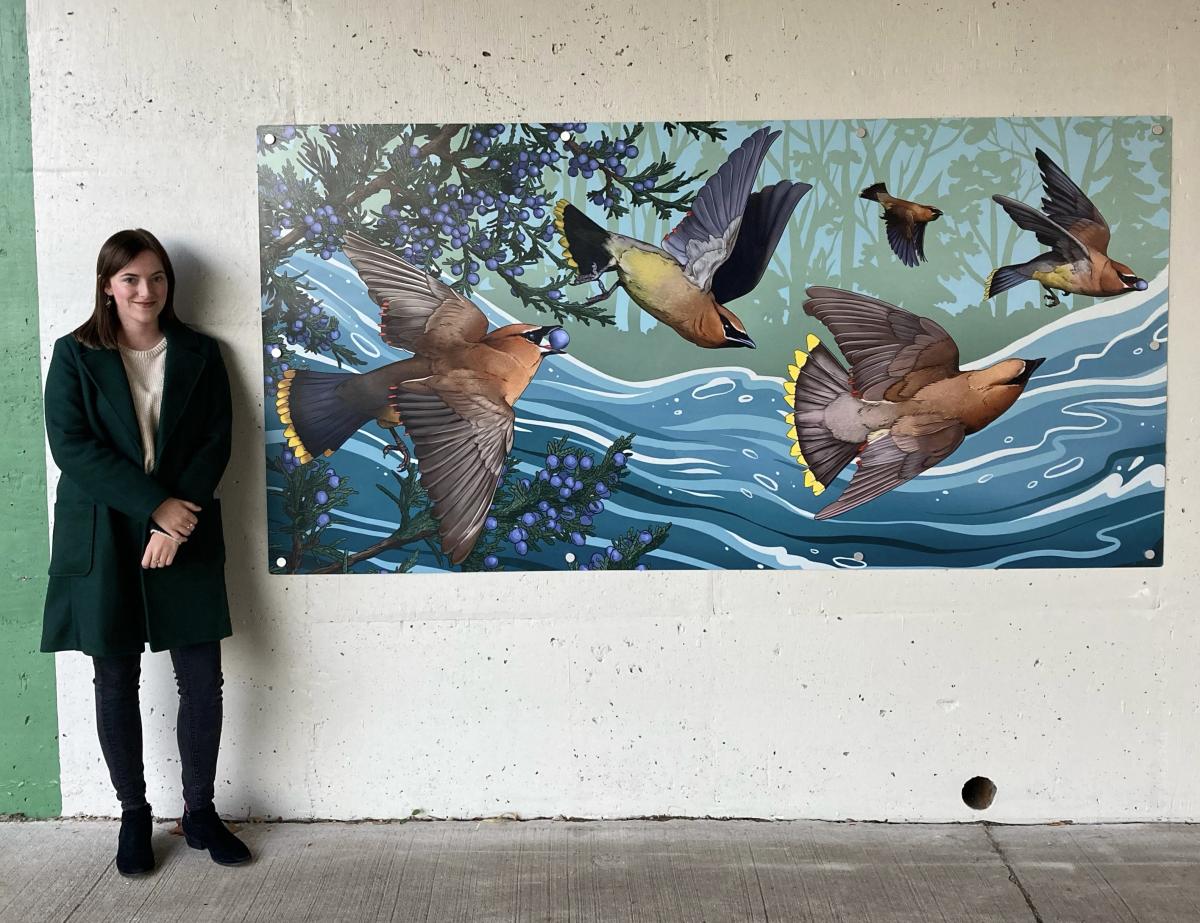 Caylin Jayde standing next to mural of Cedar Waxwings birds eating berries from trees