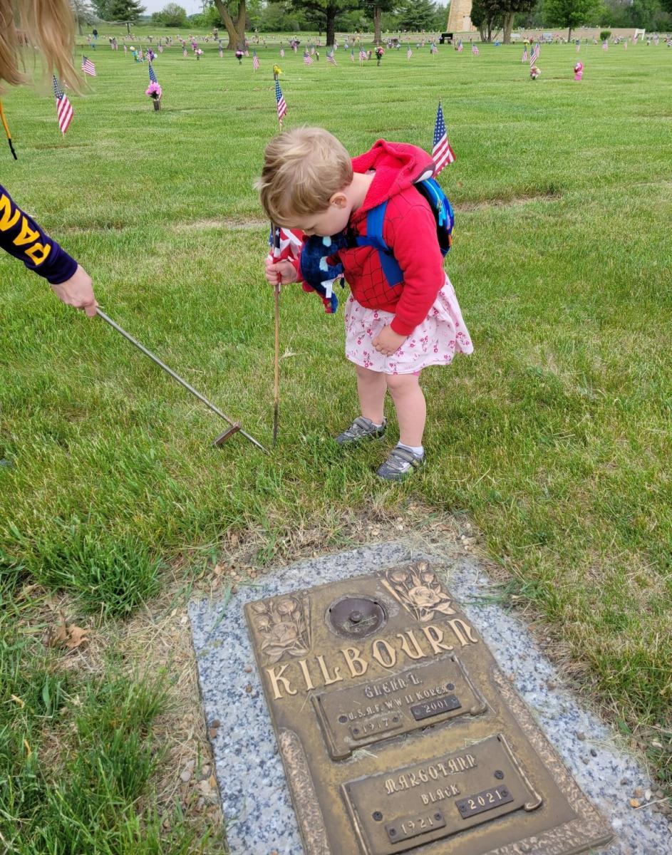 Child wearing Spiderman jacket placing flag by headstone