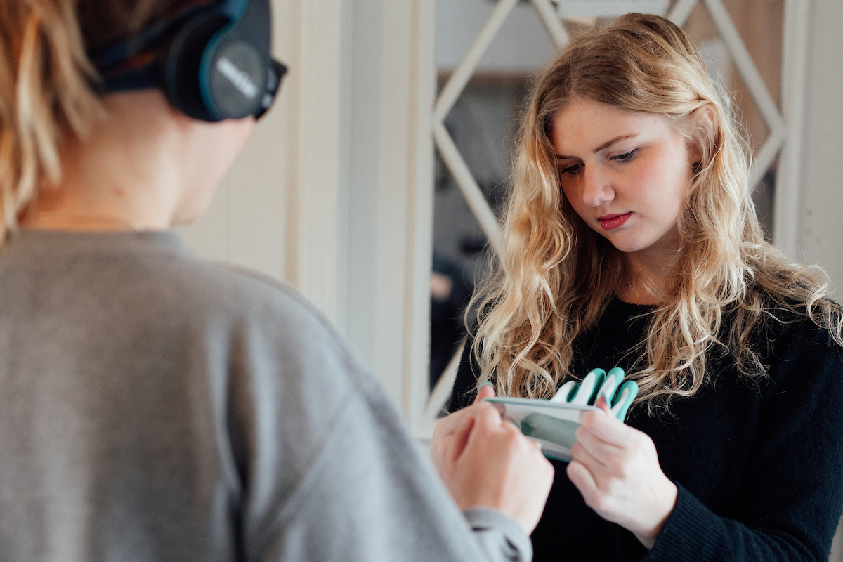 Student helps dementia simulation house attendee put on gloves