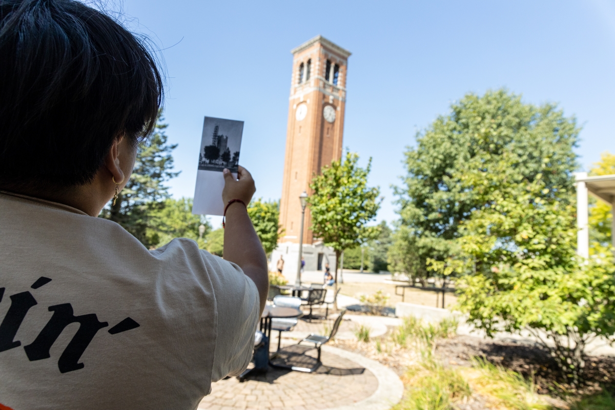 Student holding up old photo of Campanile to current Campanile