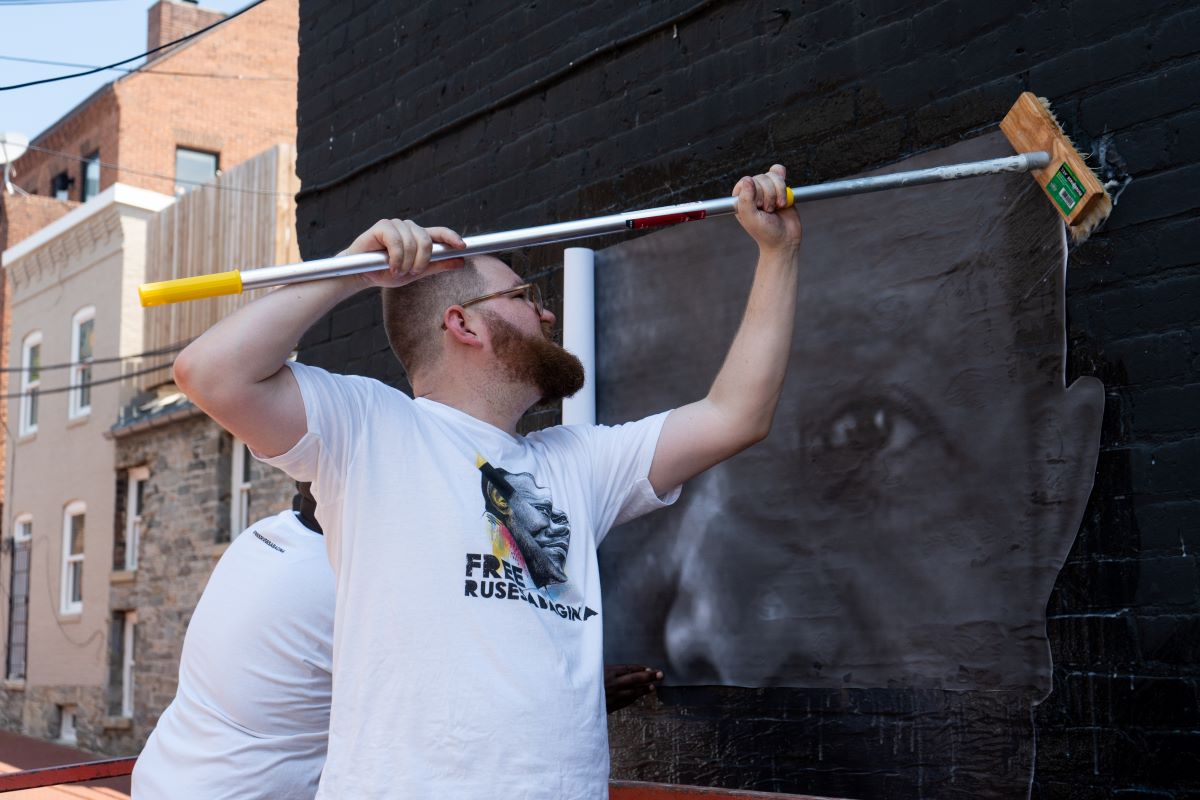 Isaac Campbell pastes photo of Paul Rusesabagina onto wall