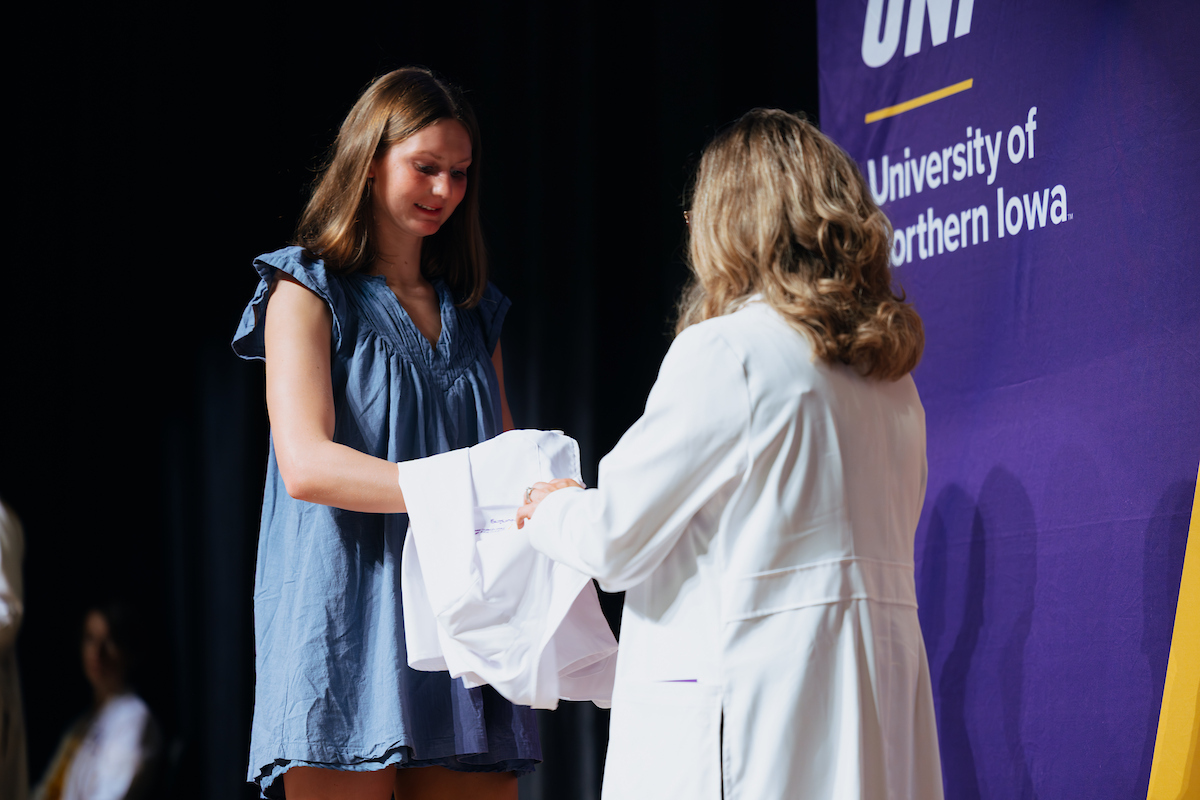 Nursing faculty member hands nursing student her white coat