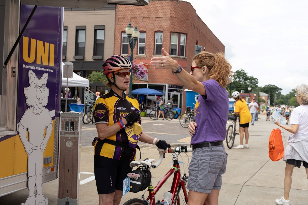 RAGBRAI rider in UNI gear getting directions from UNI employee at trailer