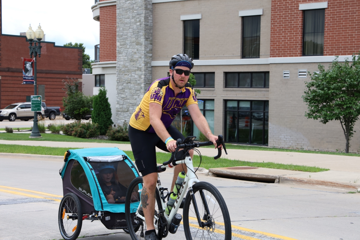 Man in UNI jersey riding bike into Cedar Falls, pulling wagon behind him