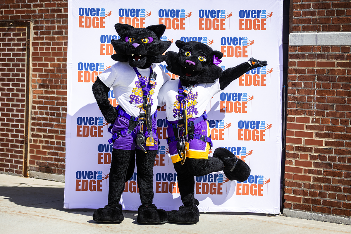 Panther duo poses for a photo in front of Over the Edge backdrop. 