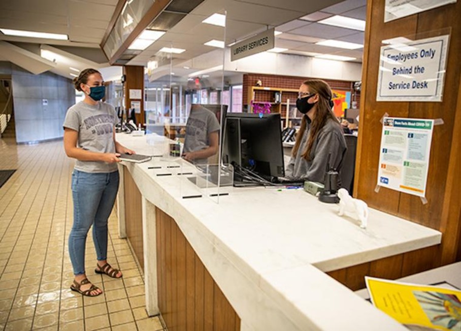 Masked UNI students interact through a Plexiglass partition in the Rod Library.