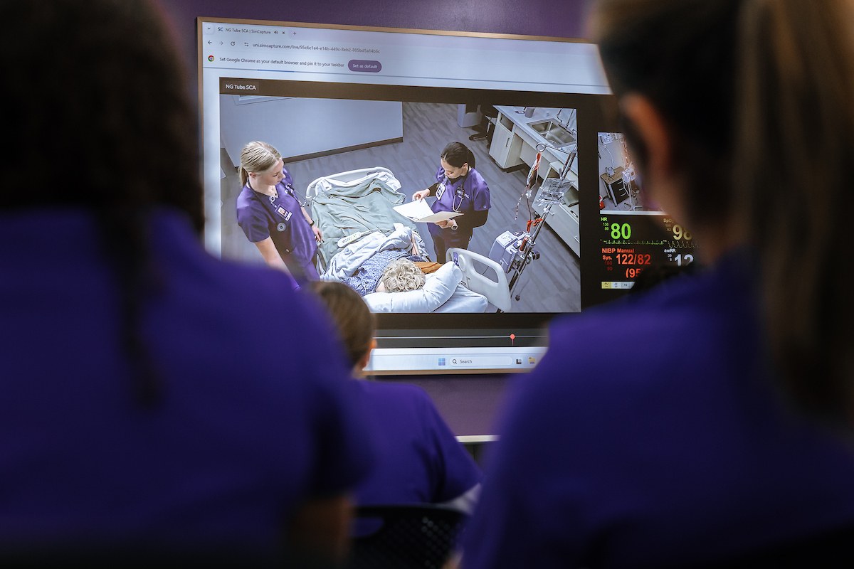 Nursing students watching other nursing students work with simulated patients through monitors