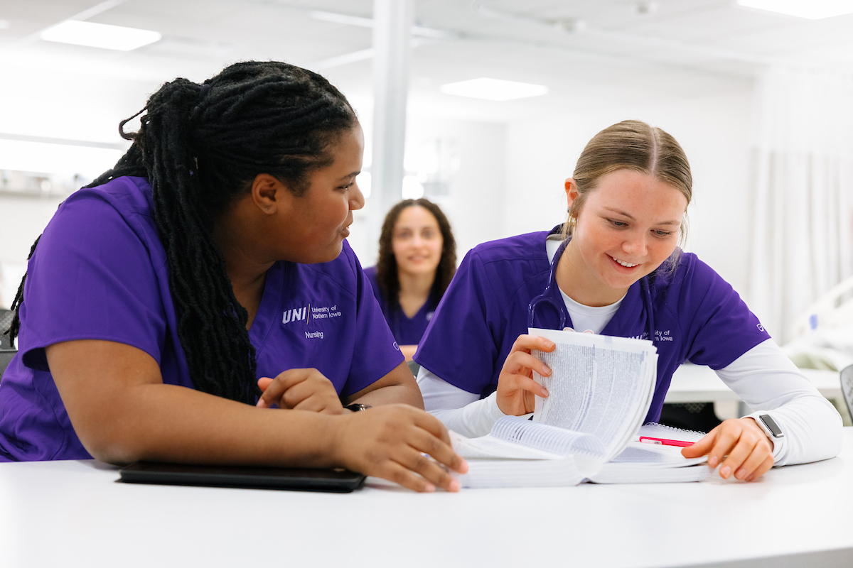 Nursing students in purple scrubs studying textbook