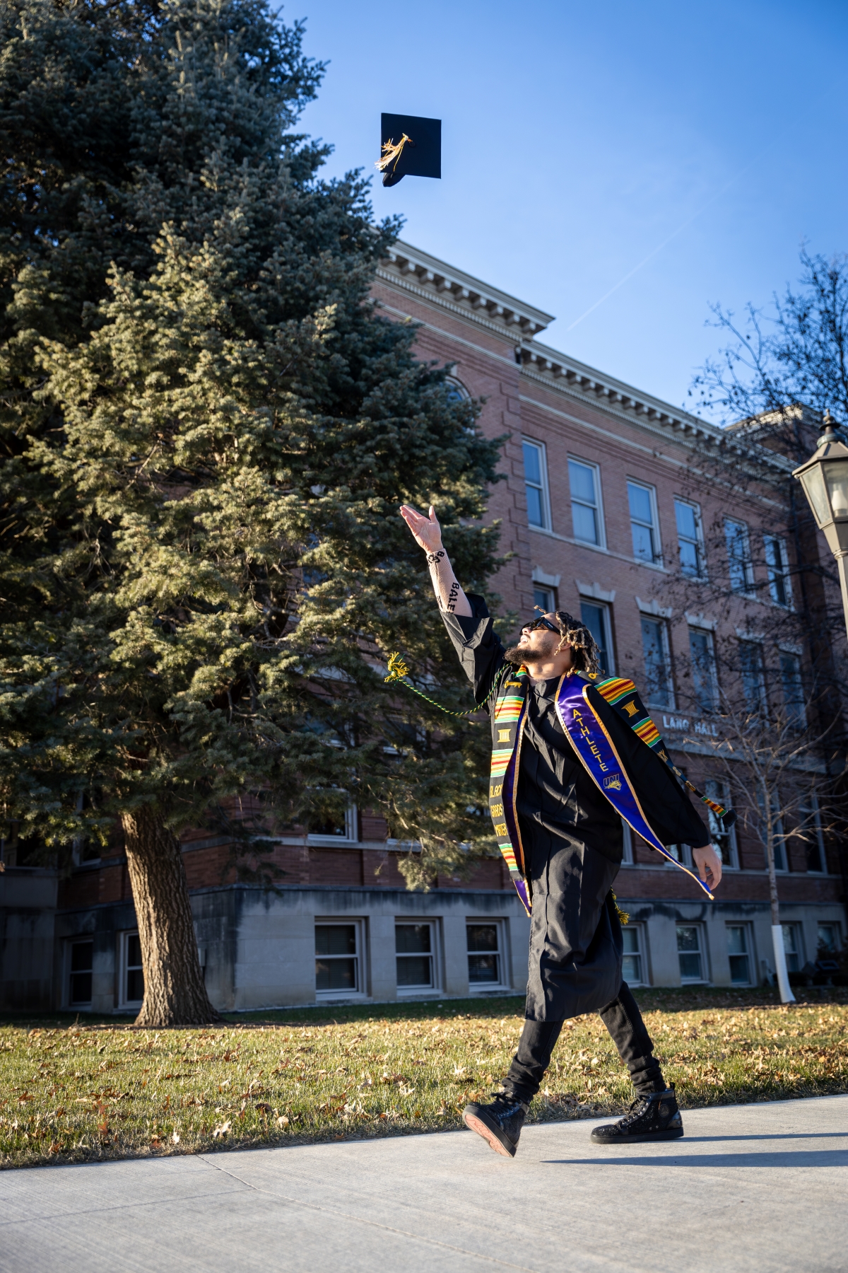 Woo Governor walking on UNI campus in graduation gown, throwing cap in the air