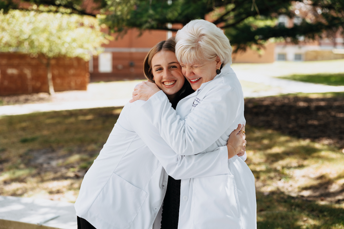 Nancy Kertz hugging new nursing student, both wearing white coats