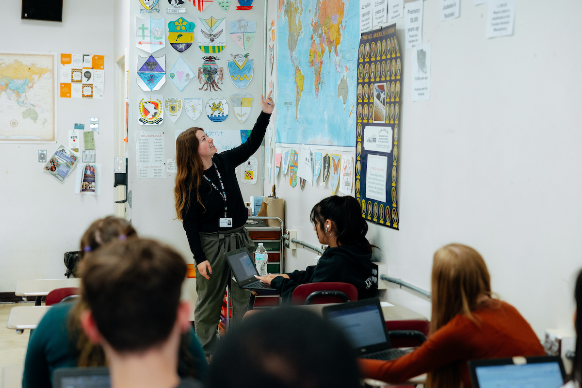 Student teacher in classroom, pointing at world map