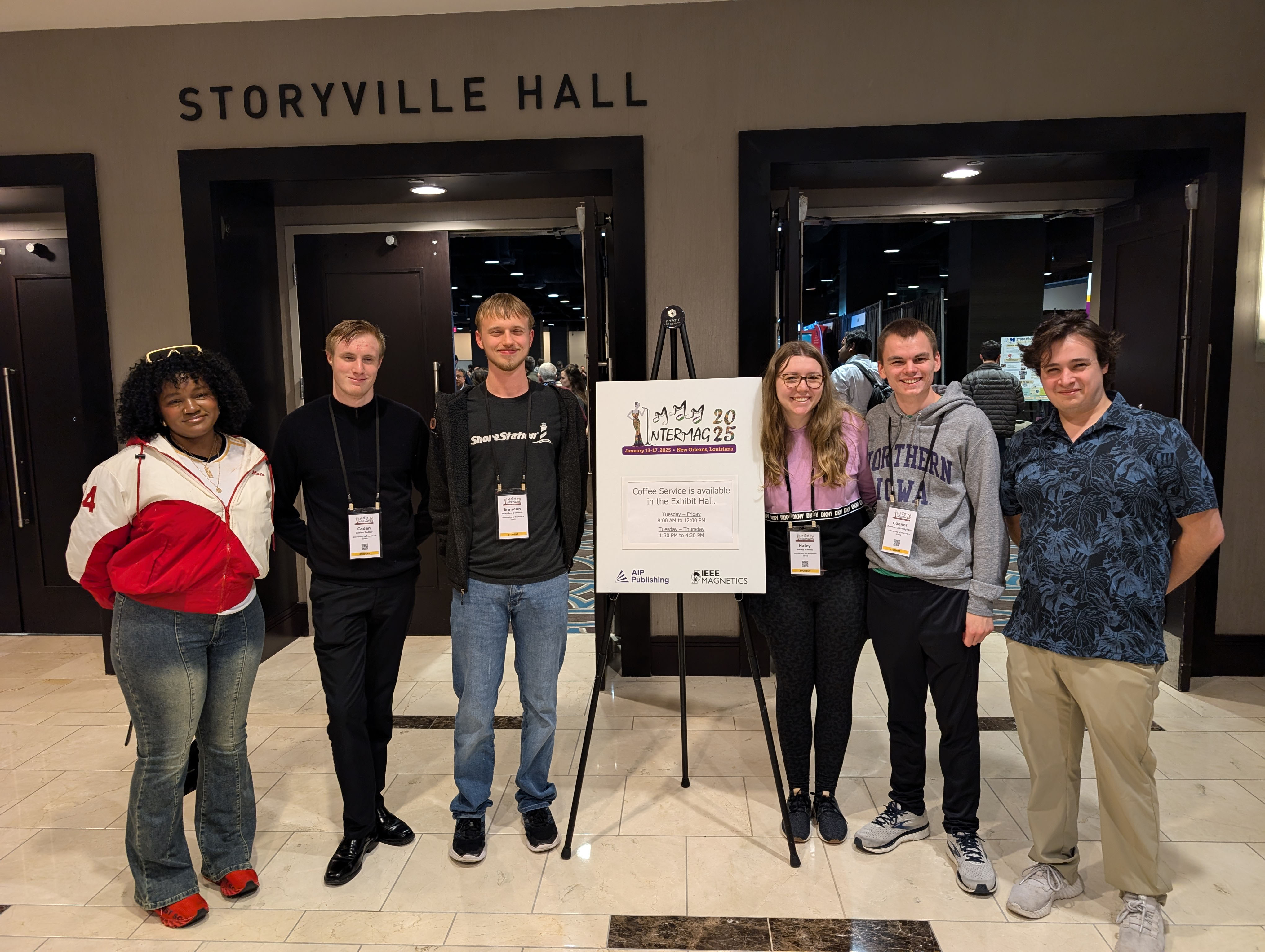 Students stand in front of a poster board presenting their work from a conference