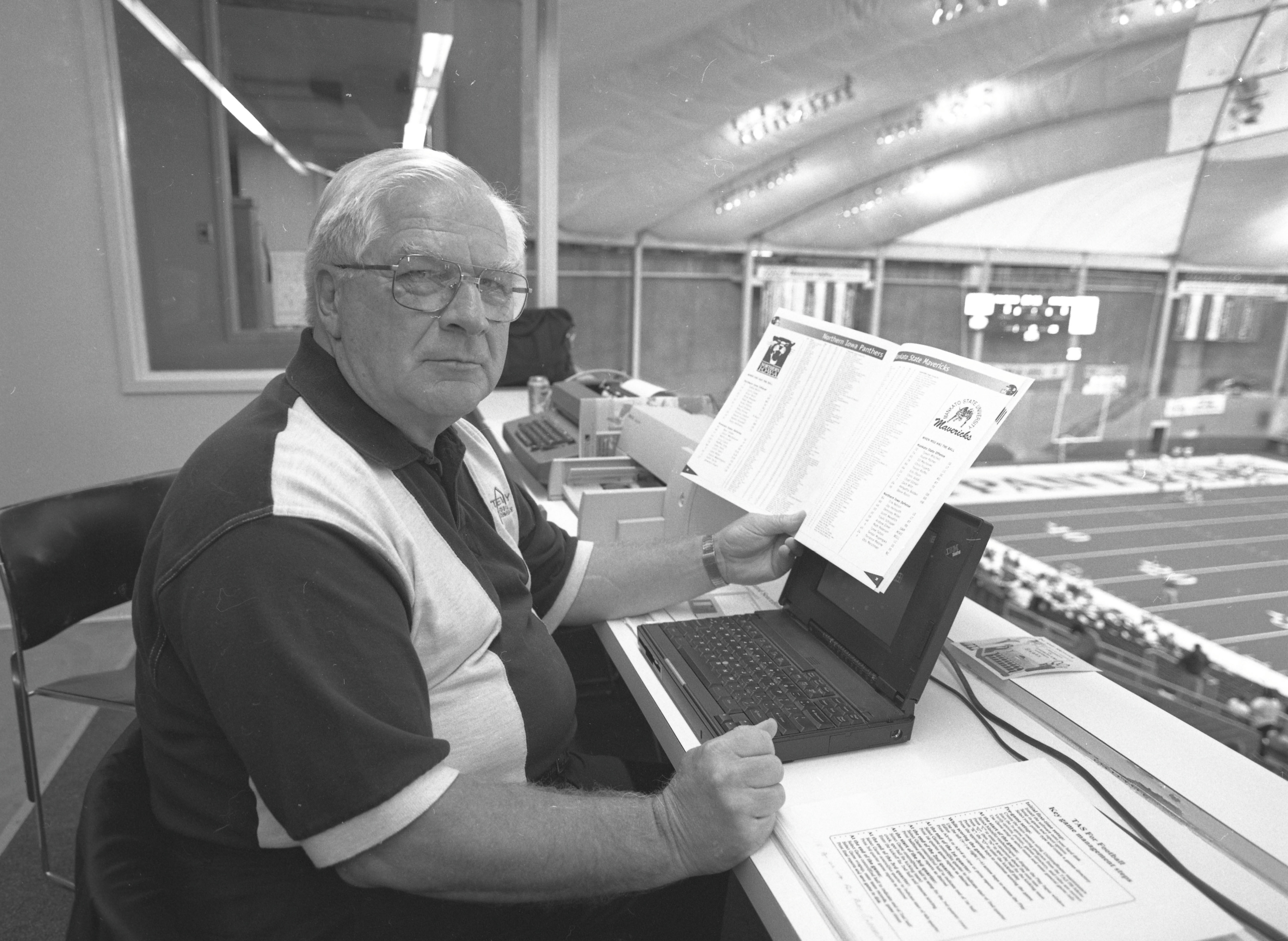 September 1997, Gaylon Halverson seated in one of the boxes overlooking the UNI-Dome field, holding a booklet and with a computer in front of him.
