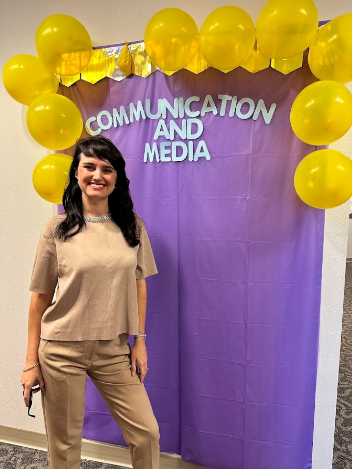 Arta Berisha standing in front of Communication and Media banner