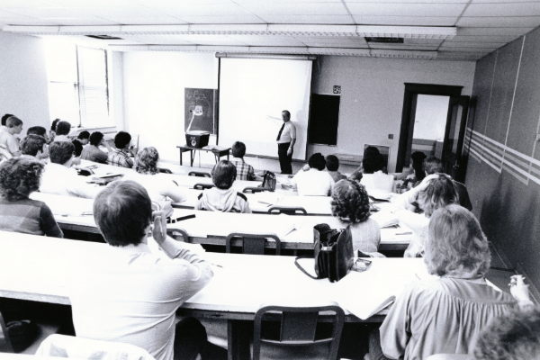 April 1980, Gaylon Halverson at the front of a classroom, teaching an accounting class using a projector.