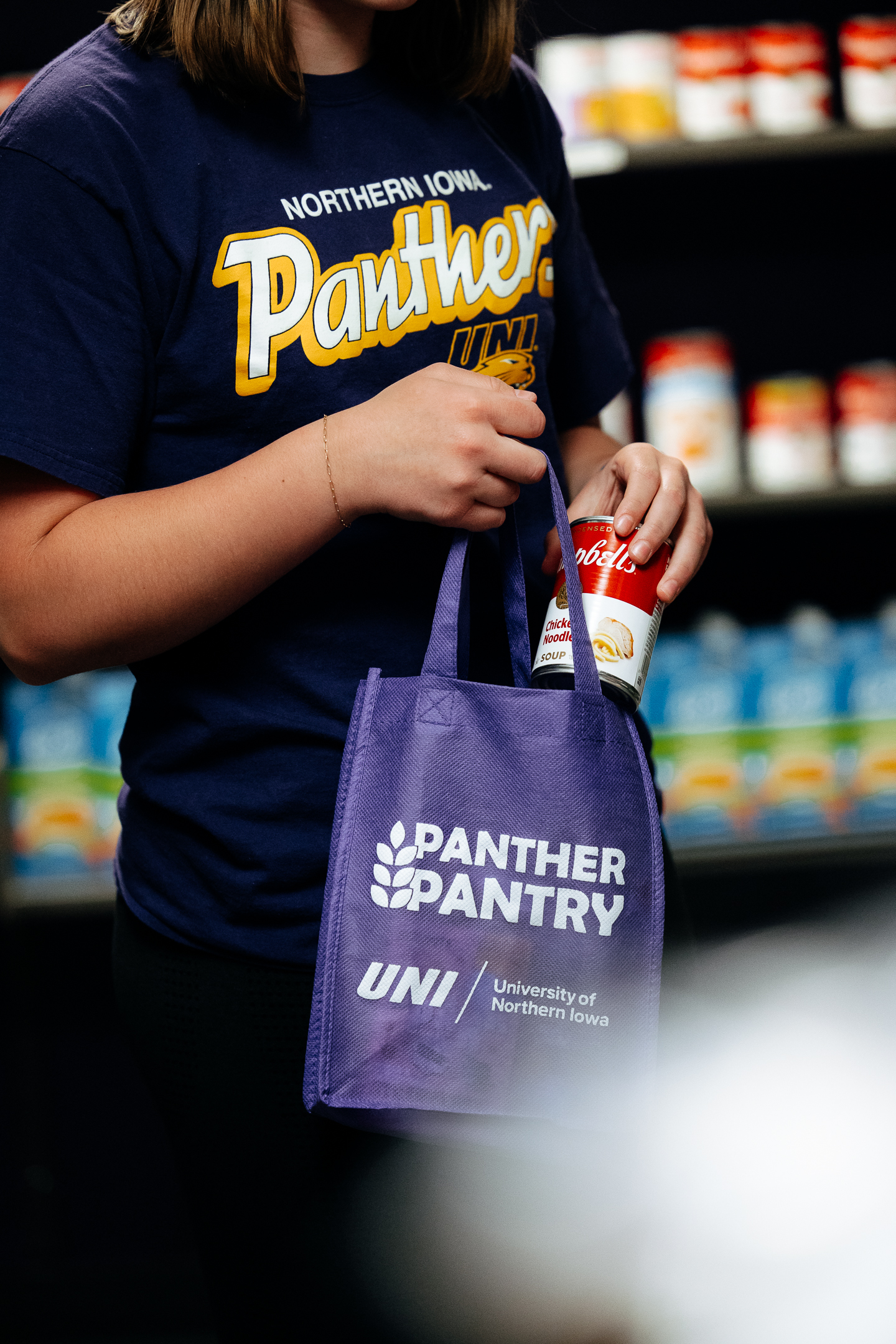 Student adding can of soup to her Panther Pantry shopping bag