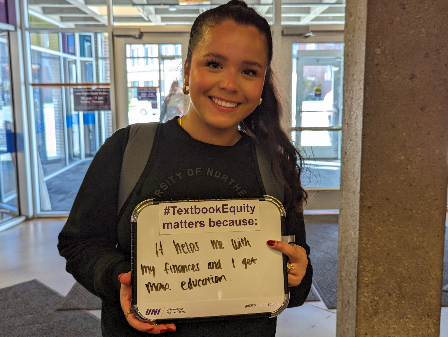 UNI student holding sign that says #TextbookEquity matters because it helps me with my finances and I get more education