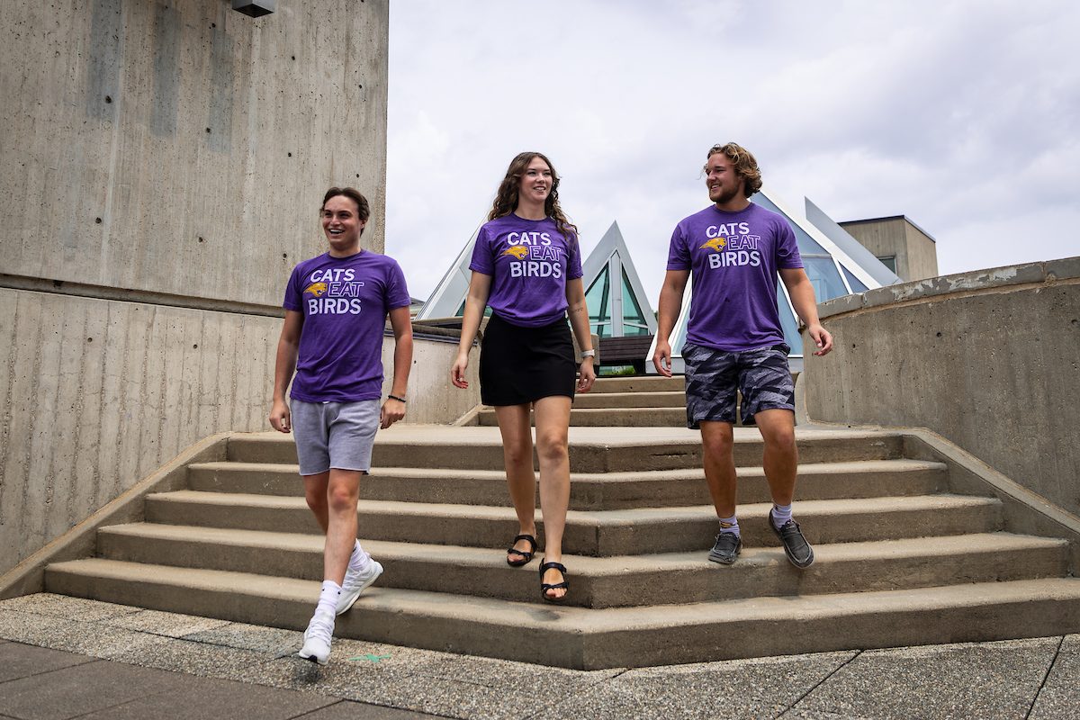 Three UNI students on campus wearing Cats Eat Birds t-shirts