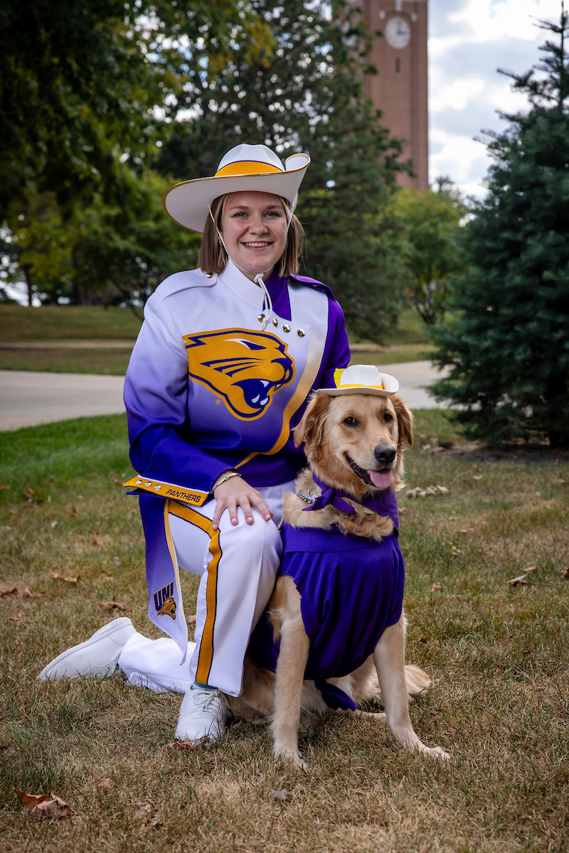 Gabi Riessen with Winnie her golden retriever service dog, both dressed in Panther Marching Band gear