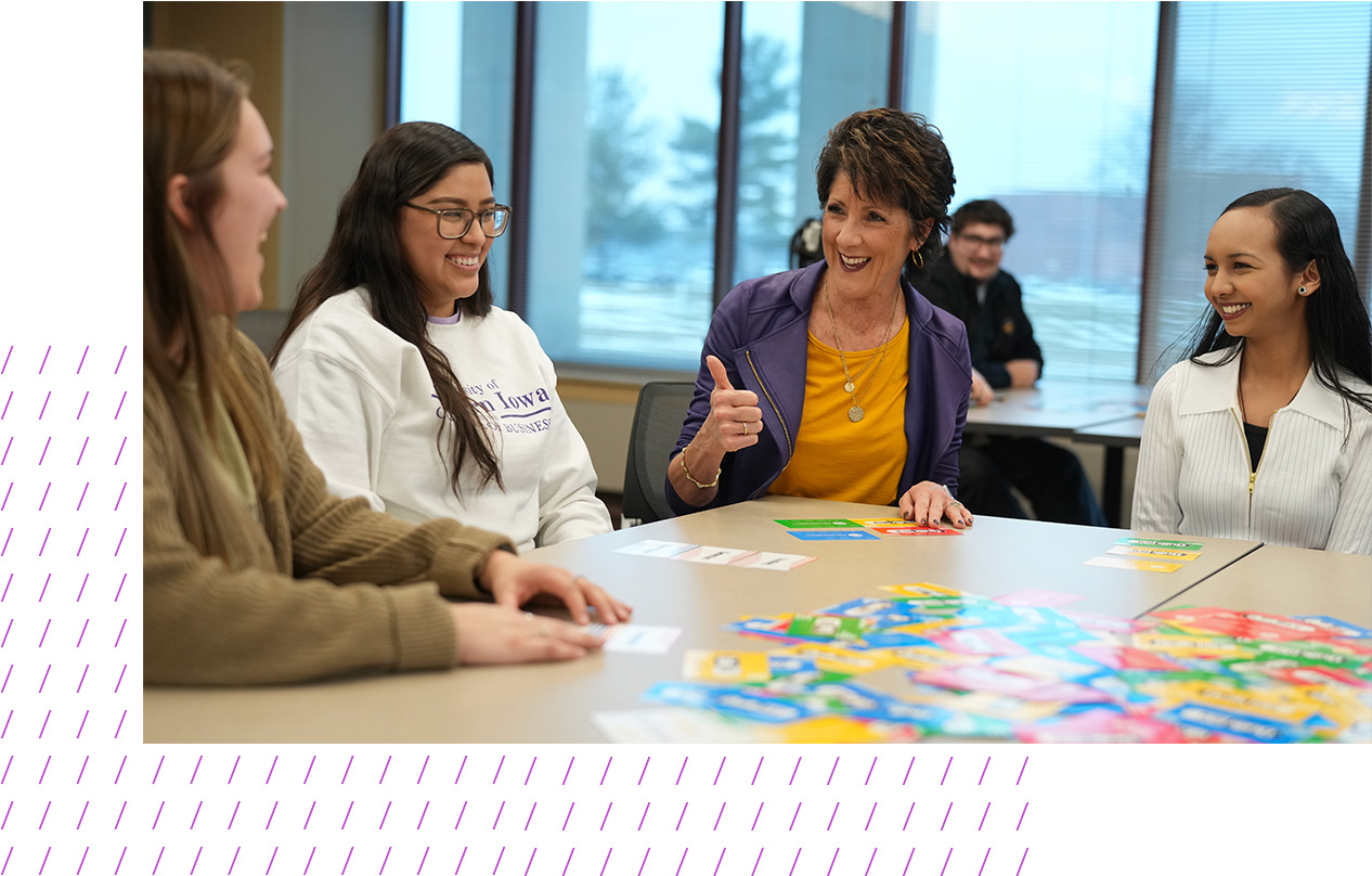 A group of college students and a faculty member sit around a table smiling and engaging in an interactive card activity as part of the Wilson College of Business Professional Readiness Program. 