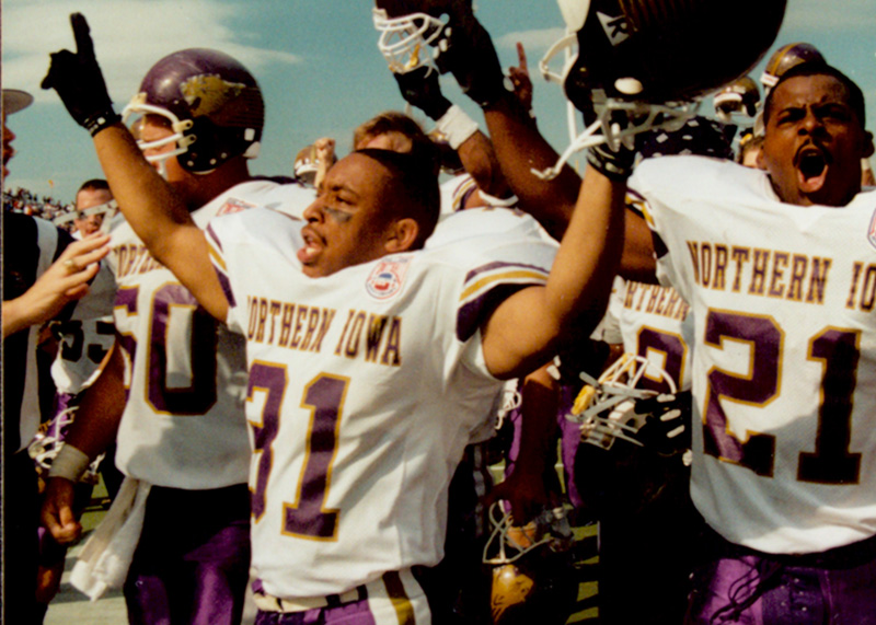 Players from the 1994 UNI Football team cheering with their helmets raised in the air
