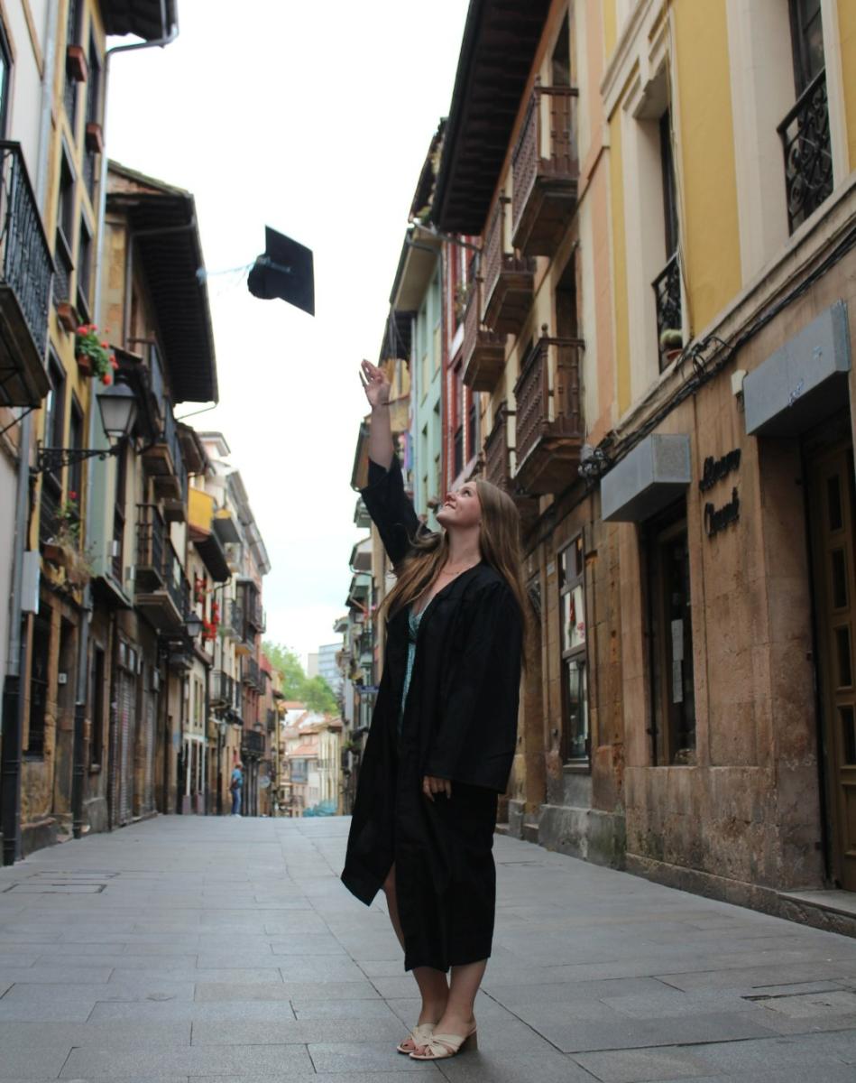 McKenna Mitchell in graduation gown throwing cap in the air in Oviedo, Spain