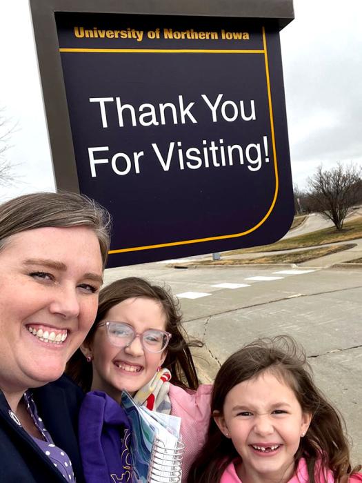 Heather Harbach and her daughters stand in front of a UNI sign