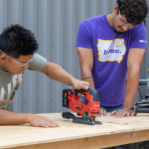 Students use saw on wood for UNI Homecoming float