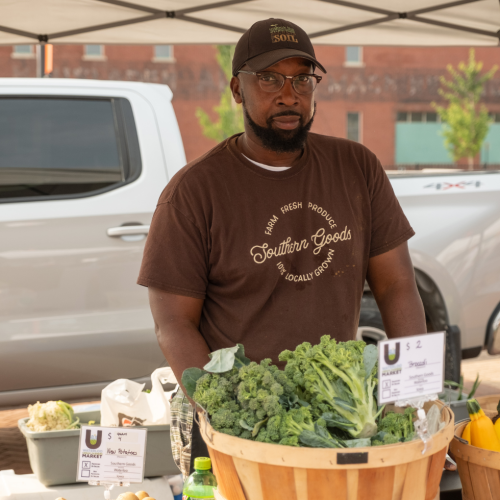 Man looking at the camera with baskets of greens in front of him.