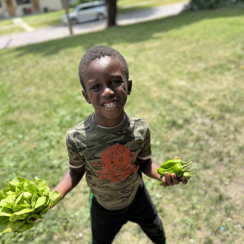 Young boy smiling and holding vegetables.