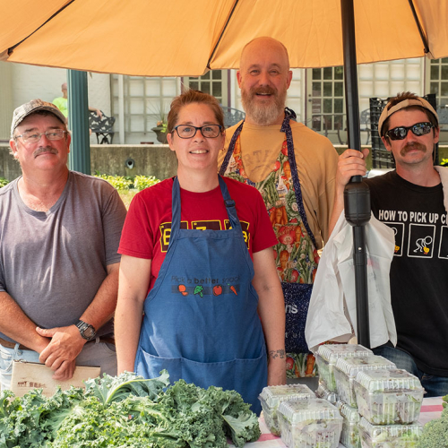 Four smiling workers selling vegetables.