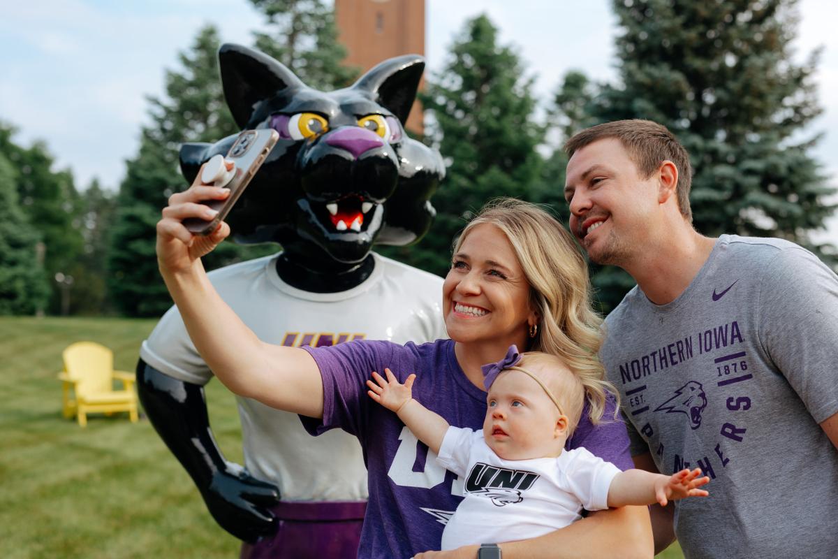 Family dressed in Panther gear taking a selfie in front of TC statue on UNI campus