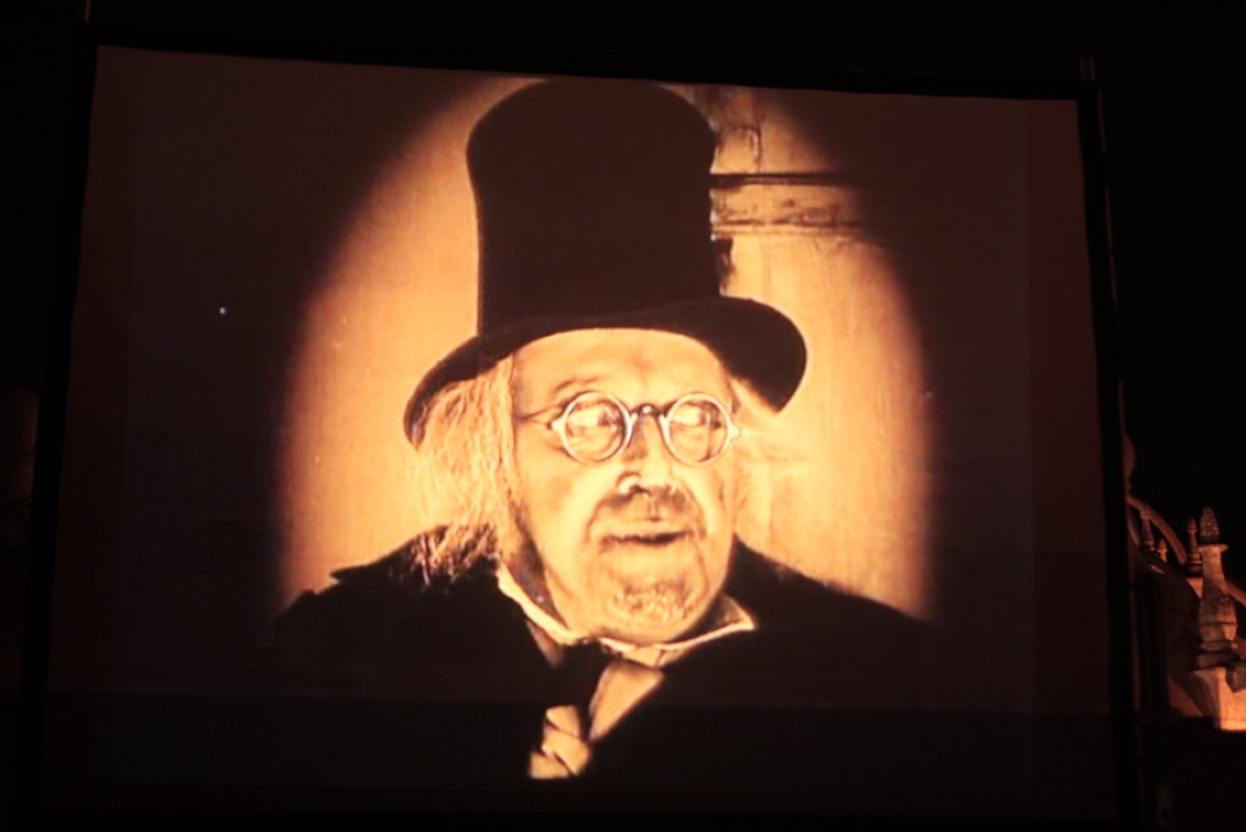 Man with a top hat and glasses in dim light looking off to the side