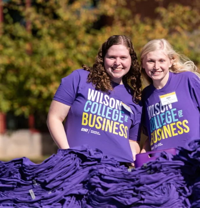 Two students wearing Wilson College of Business t-shirts, passing otu t-shirts to students