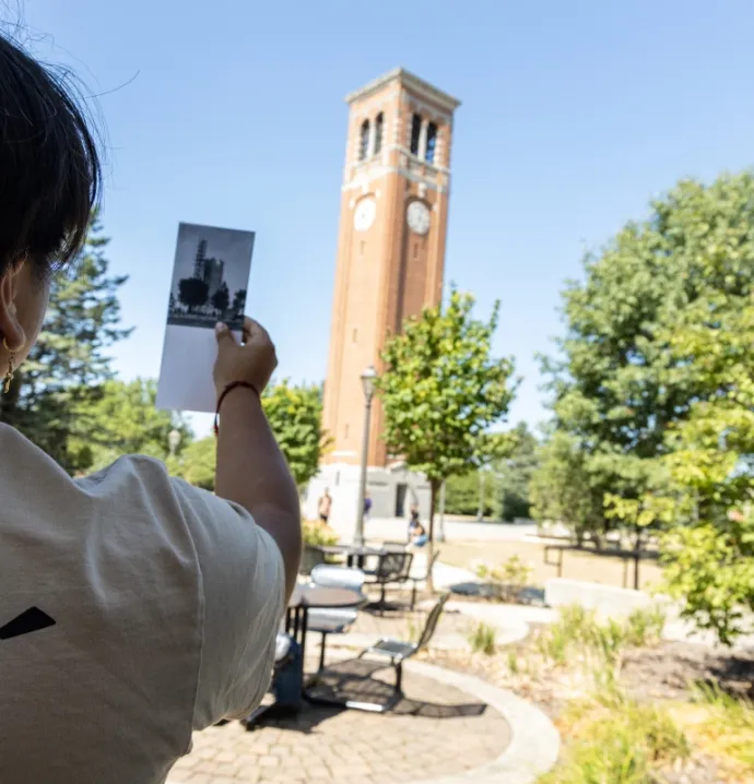 Person holding up old photo of the Campanile to compare it to the current Campanile
