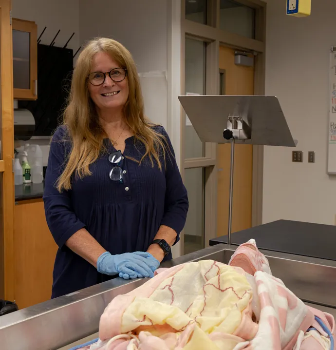 UNI instructor, Mary McDade, standing next to a synthetic cadaver used in the syndaver lab.