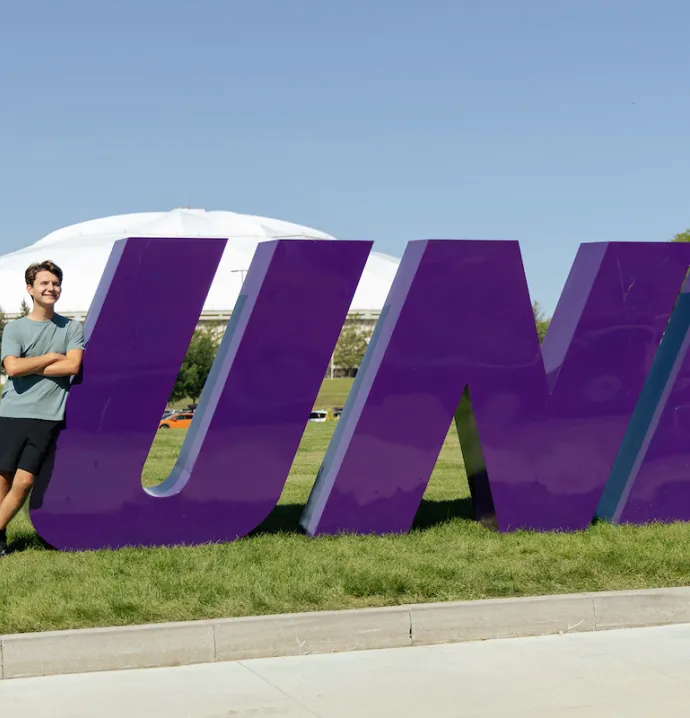 UNI student leaning against UNI sign