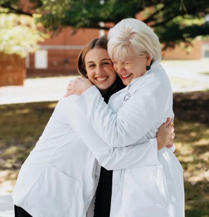 Nancy Kertz hugging new nursing student, both wearing white coats