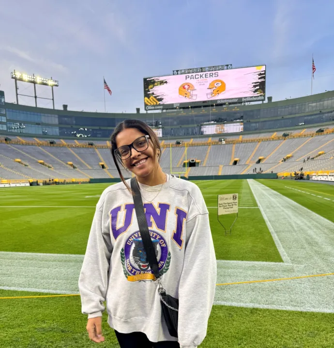 Adamari Barranca standing with a UNI sweatshirt in an empty Lambeau Field