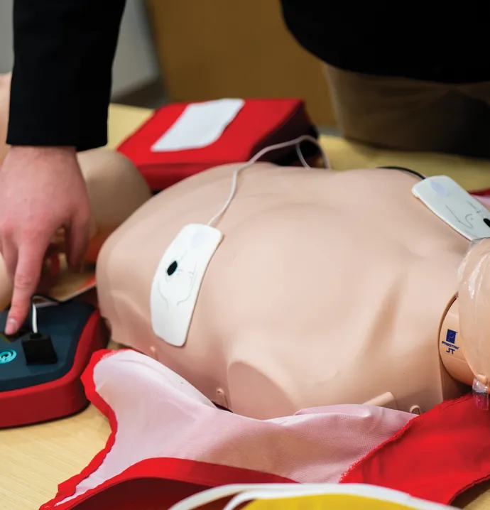 A person practices using an AED on a CPR training mannequin.