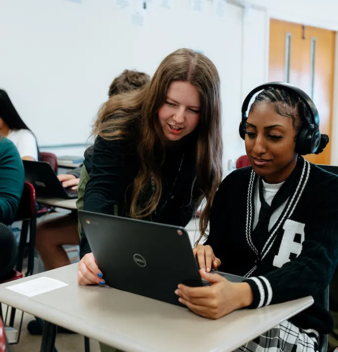 Teacher education student helping one of their students with a laptop at their desk