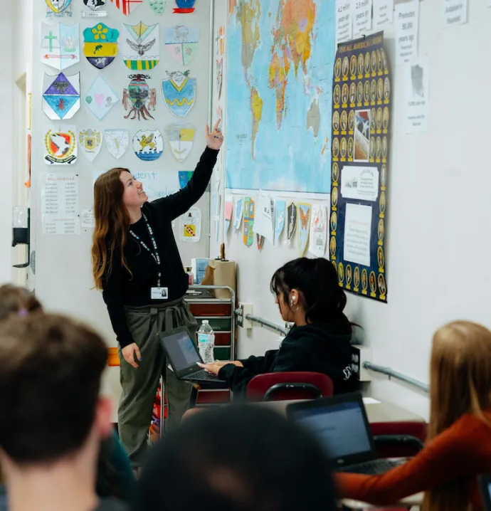 Student teacher in classroom pointing at world map