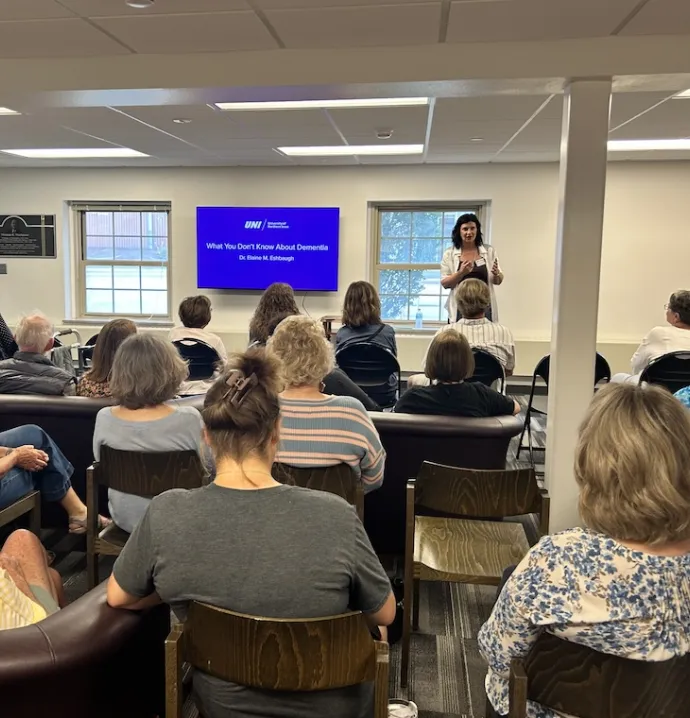 Prof. Eshbaugh speaking at seminar in front of a room of people. "What you don't know about Dementia" displayed on screen behind her.