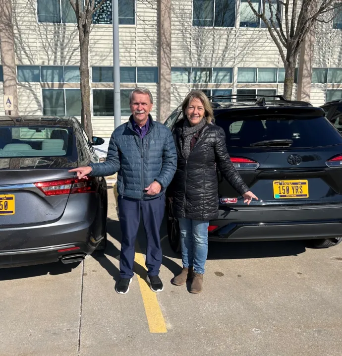 Randy Pilkington and Cary Darrah pointing at their custom license plats that say "UNI 150" and "150 YRS"