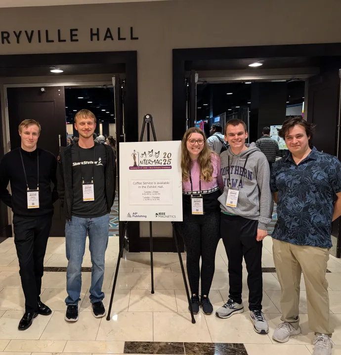 Students stand in front of a poster board presenting their work from a conference