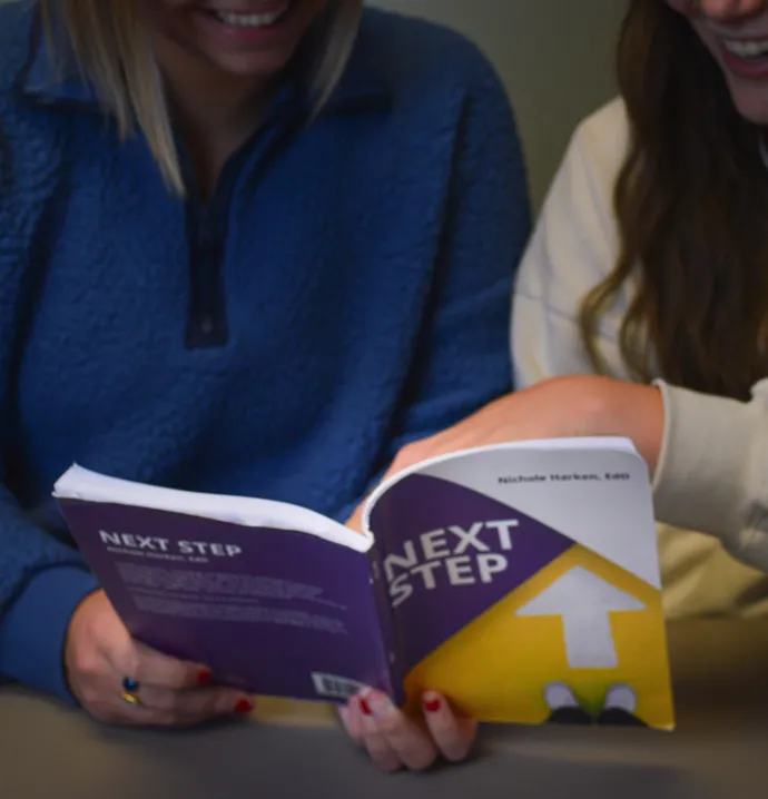 Two students looking at a copy of the Next Step textbook