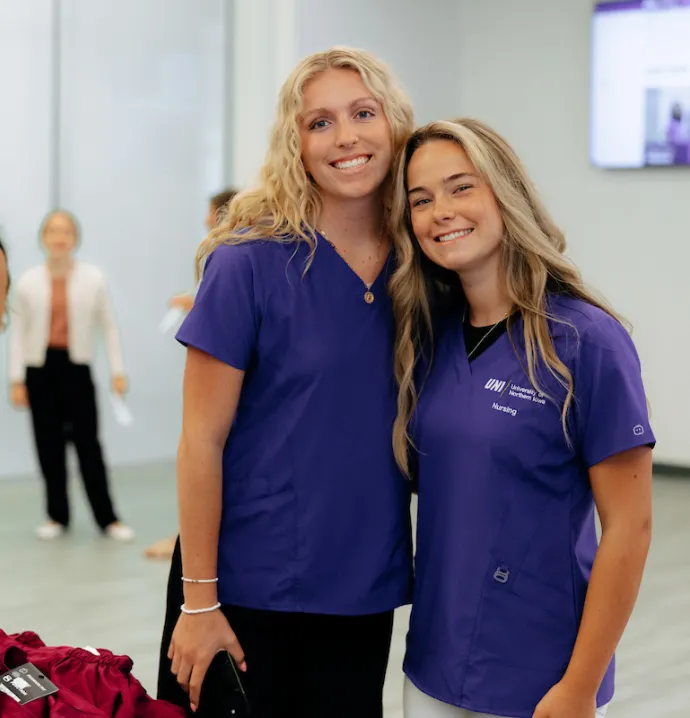 Two UNI nursing students wearing their purple scrubs
