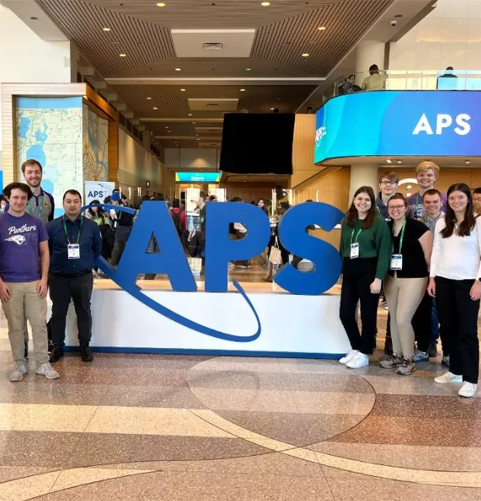 Students standing in front of an APS sign at convention 