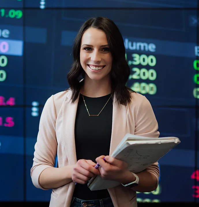 Student holding notebooks in front of a stock market display, representing a finance degree and double major career opportunities
